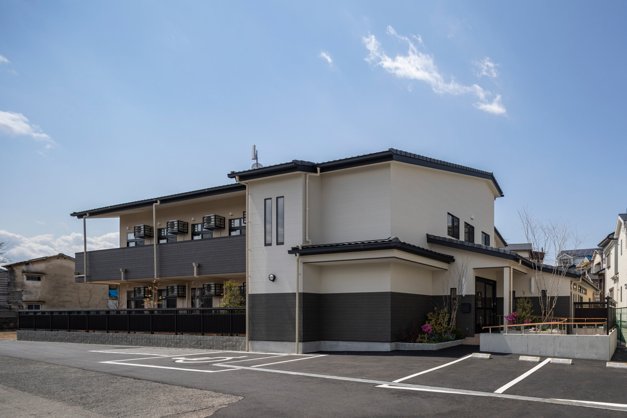 介護施設の建物外観。モダンな和風デザインの2階建て施設で、駐車場を備えている。
